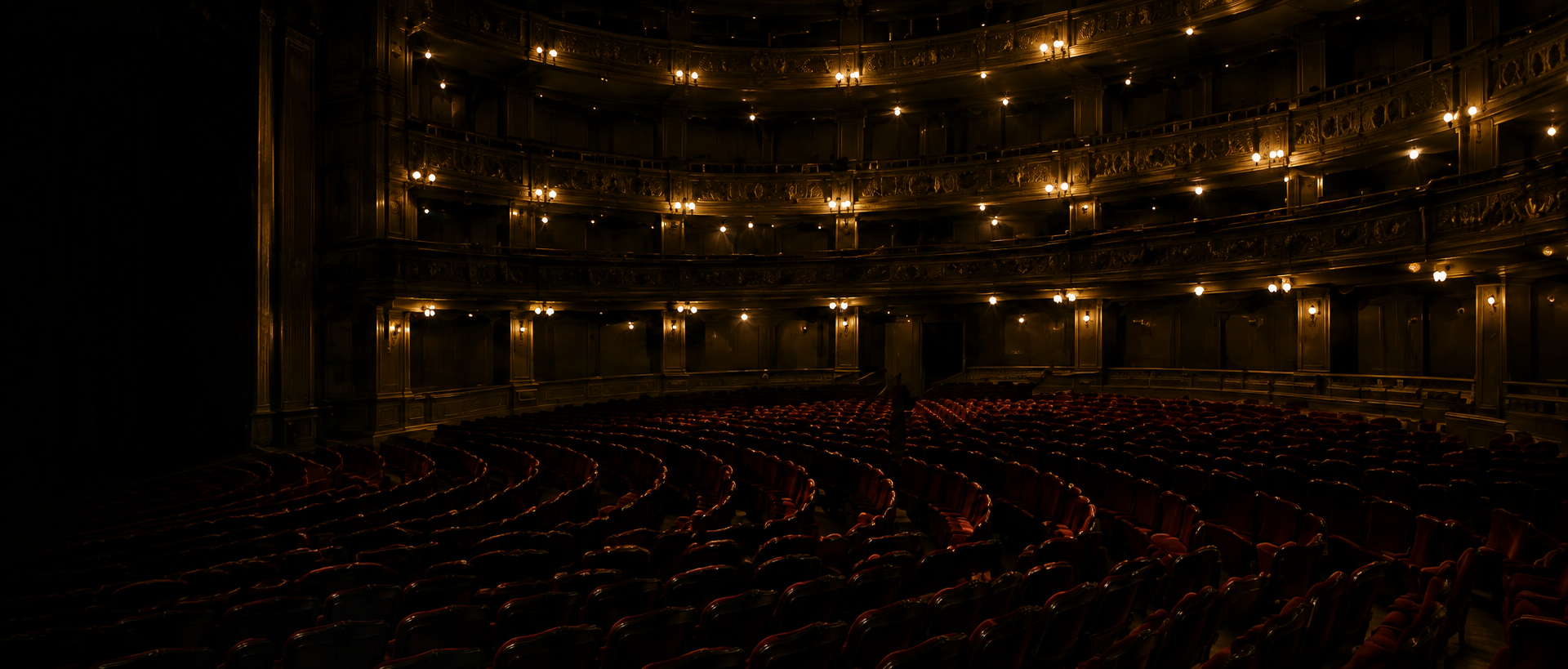 An ornate theatre auditorium with rows of red seats and golden balconies